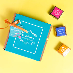 CAROLINAS BOX WITH BLUE SLEEVE AND RIBBON AND MOTHERS DAY TAG. ON THE SIDE, THREE BROWNIES WITH COLOURFUL LABELS