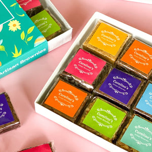 Open box of Carolina's brownies with colourful labels on them and on the left up corner a piece of the closed box is showing
